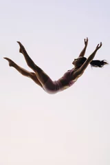 Fotobehang In-flight gymnast: A female acrobatics performer leaps mid-air in a graceful routine © Jacob Lund