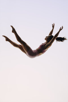Fototapeta In-flight gymnast: A female acrobatics performer leaps mid-air in a graceful routine
