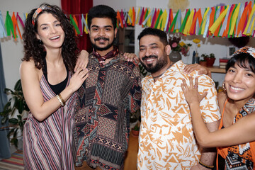 Fototapeta na wymiar Two happy young affectionate couples in national attire looking at camera with smiles while standing in home environment and enjoying party