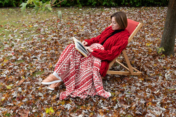 A woman sits on a bench on the backyard as she gets lost in the pages of her book. The autumn leaves, a vibrant yellow fall gently and creating a picturesque scene