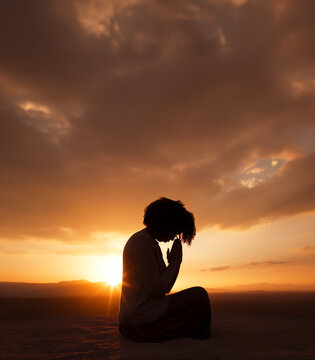 Prayer concept. Silhouette of a pretty black woman in a praying pose. Set against a vibrant sunset sunrise sky. Clasped hands. Also related to reverence, anointing, Pentecost, sacrament, authority