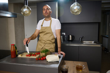 Portrait of a Caucasian middle aged man, a chef in beige apron, standing at kitchen counter with...