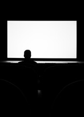 Silhouette of a man, a lone spectator sitting in a chair in the cinema hall against a white screen, rear view black and white photo