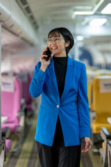 Confident businesswoman in blue blazer talking on a smartphone while walking down the airplane...