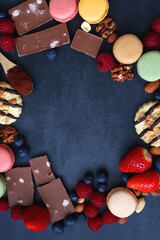 Macarons, chocolate, cookies, berries and various nuts on dark blue background. Top view.