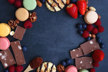 Macarons, chocolate, cookies, berries and various nuts on dark blue background. Top view.