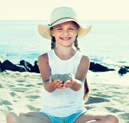 Baby girl in hat playing with sand on sea coast in summer