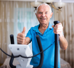 Mature man exercising on an elliptical machine and showing thumb up