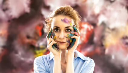 Woman Painter of abstract paintings painted with paints on her face, posing in front of her painting - 782160517