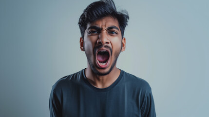 An Indian young man screaming out of frustrations against a light grey gradient background