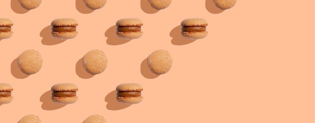 Beige color macaroons cookies on a peach fuzz background with shadows. Macaron cookies. Space for text. Monochrome image. Minimal food dessert concept. Copy space. Banner or header