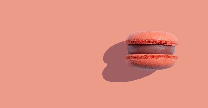 Coral color macaroons cookies on a coral background with shadows. Space for text. Minimal food dessert concept. Copy space. Banner