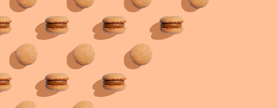 Beige color macaroons cookies on a peach fuzz background with shadows. Space for text. Minimal food dessert concept. Copy space. Banner