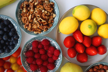 Apples, lemons, bananas, berries, carrots, leek, tomatoes, radishes, spinach and various nuts on white background. Healthy seasonal fruit and vegetable. Top view.