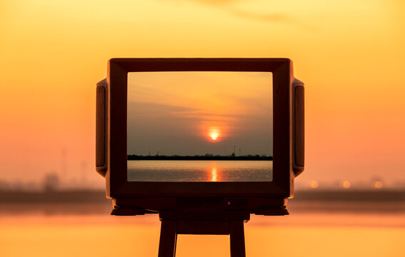 Silhouette of TV frame on bench with beautiful sunset at the lake.
