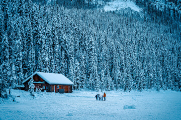 Banff, Canada in the winter with a family making a snowman by a cabin.