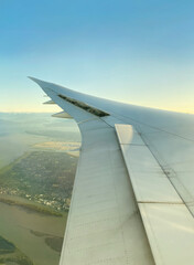 View from airplane window. Wing of an aircraft. Aerial view of a city with green land. The white wing of the plane with the earth below.