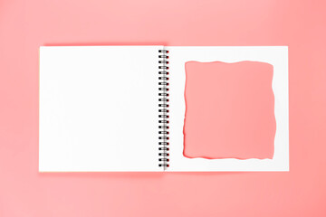 White notebook with cut-out frame on the page. Blank layout template of spiral notebook on pink background.