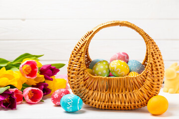 Easter basket filled with colorful eggs and a bouquet of tulips on a textured wooden table. Easter celebration concept. Colorful easter handmade decorated Easter eggs. Place for text. Copy space