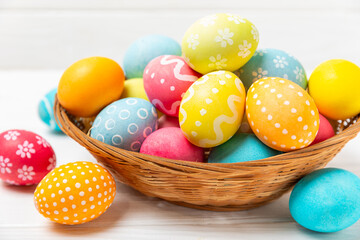 Easter basket filled with colorful eggs and a bouquet of tulips on a textured wooden table. Easter celebration concept. Colorful easter handmade decorated Easter eggs. Place for text. Copy space