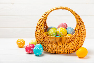 Easter basket filled with colorful eggs and a bouquet of tulips on a textured wooden table. Easter celebration concept. Colorful easter handmade decorated Easter eggs. Place for text. Copy space