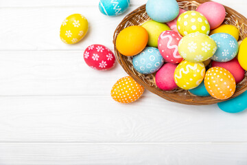 Easter basket filled with colorful eggs and a bouquet of tulips on a textured wooden table. Easter celebration concept. Colorful easter handmade decorated Easter eggs. Place for text. Copy space