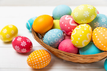 Easter basket filled with colorful eggs and a bouquet of tulips on a textured wooden table. Easter celebration concept. Colorful easter handmade decorated Easter eggs. Place for text. Copy space