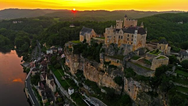 Cinematic panoramic view of feudal square-shaped castle on a riverside clifftop at golden sunset in France. Aerial view of Ch&acirc;teau de Beynac fortress at golden hour in France.