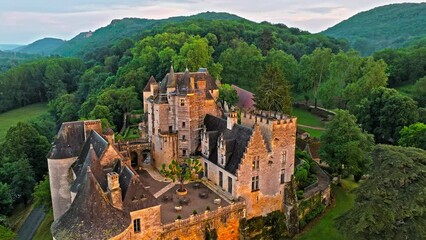 Cinematic panoramic view of feudal square-shaped castle on a riverside clifftop at golden sunset in France. Aerial view of Château de Beynac fortress at golden hour in France.