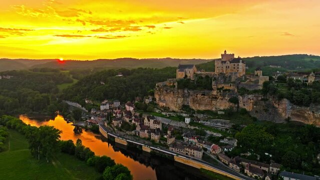 Cinematic panoramic view of feudal square-shaped castle on a riverside clifftop at golden sunset in France. Aerial view of Ch&acirc;teau de Beynac fortress at golden hour in France.
