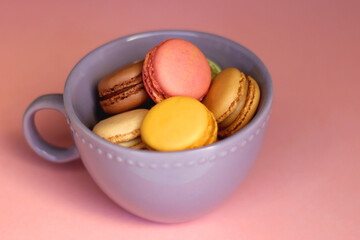 Purple cup filled with pastel macarons on pink background. Selective focus.