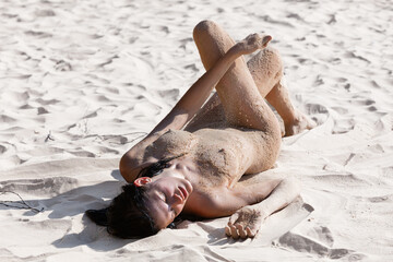 Young woman posing nude on a sandy beach