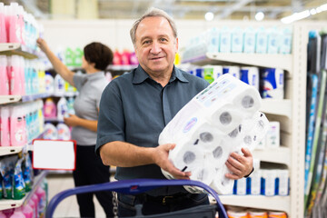 Elderly man chooses toilet paper in supermarket