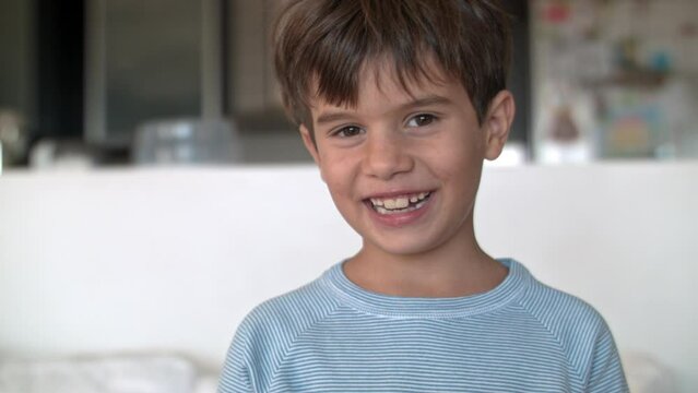 Portrait of a young boy in a blue shirt sitting inside a bright room