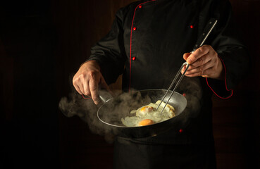 Cropped silhouette of a chef with a hot frying pan for cooking scrambled eggs for breakfast....