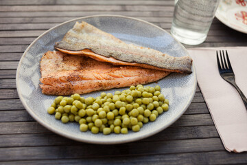 Top view of baked trout fillet served on plate with peas closeup