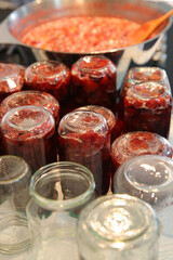 Cooking strawberry jam in a large bowl at home. Wooden spoon in a bowl with jam. Empty glass jam jars and jars filled with jam.