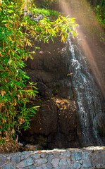Imagen vertical de una cascada pequeña en la naturaleza con rocas y una luz del sol 