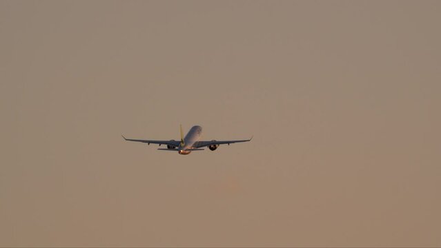 An airplane with elongated wings and an illuminated tail, flying against the background of the evening sky with a gradient, at dusk