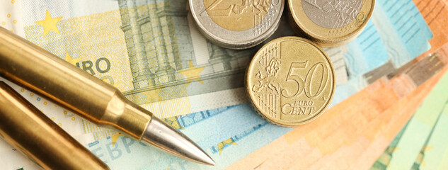 Yellow cartridges and shell casings on euro banknotes. Lot of bills of European union currency and ammo close up