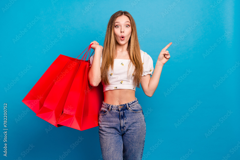 Sticker Photo of shocked girl hold shopping bags point finger empty space isolated blue color background