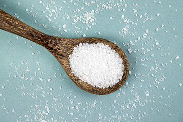 Sea salt grains on wood spoon and scattered around blue background, lot of copy space. Studio shot.