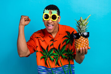 Photo of cheerful lucky guy dressed print shirt rising fist holding pineapple wear dark glasses...