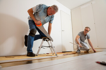 Two mature men installing laminate flooring in a new home together. DIY concept. Professional...