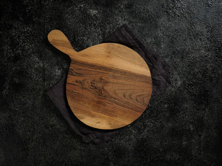 Top view of empty round wooden cutting board with handle on beautiful dark background.