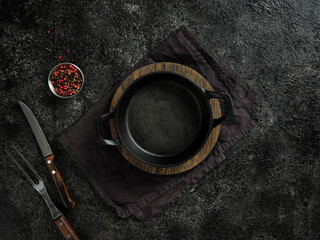 Top view of an empty black cast iron frying pan on a wooden board and a cloth towel.