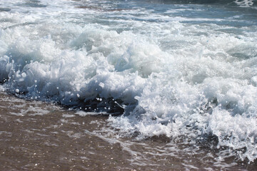 Sea water with white foam on the beach on a sunny day, wave with foam