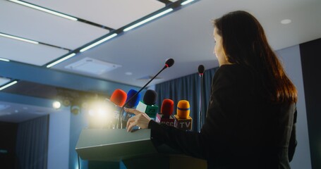 Female press officer pronounces speech from tribune during press campaign in the conference hall....