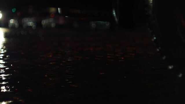 Night road in the city made of paving stones during a rainstorm. In the foreground you can see a piece of a parked car.