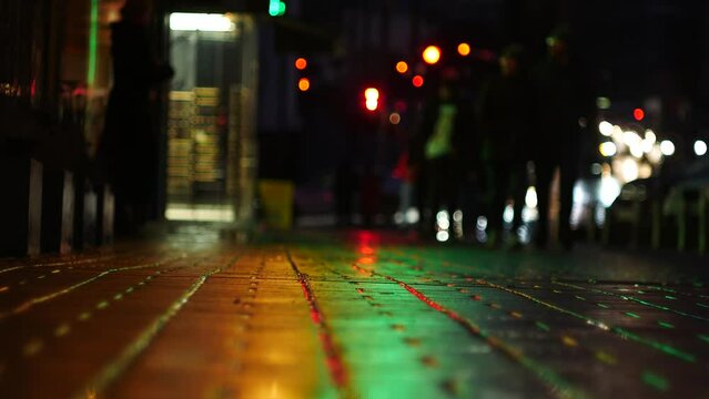 People walk along the wet sidewalk during the night rain. In the background you can see many blurred car headlights.